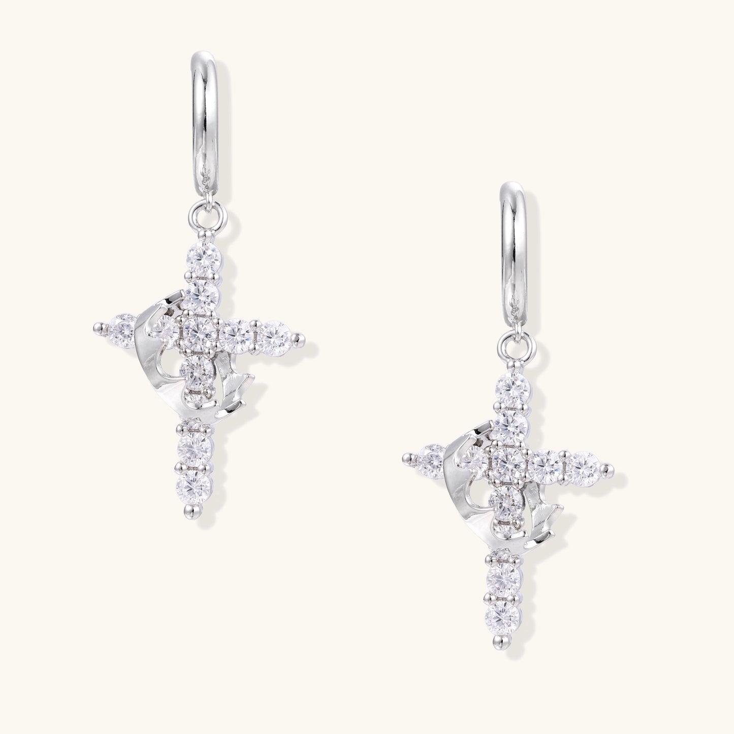 White gold-plated hoop earrings with sparkling zirconia cross charms dangling against cream background