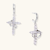 White gold-plated hoop earrings with sparkling zirconia cross charms dangling against cream background