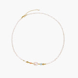 Delicate white beaded necklace with baroque pearl center, gold accents, and coral and aqua gemstones on cream background.