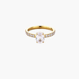 Gold-plated solitaire ring with oval zirconia center stone and pavé band on cream background