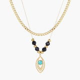Layered gold necklace with turquoise evil eye pendant and black quartz beads on cream background