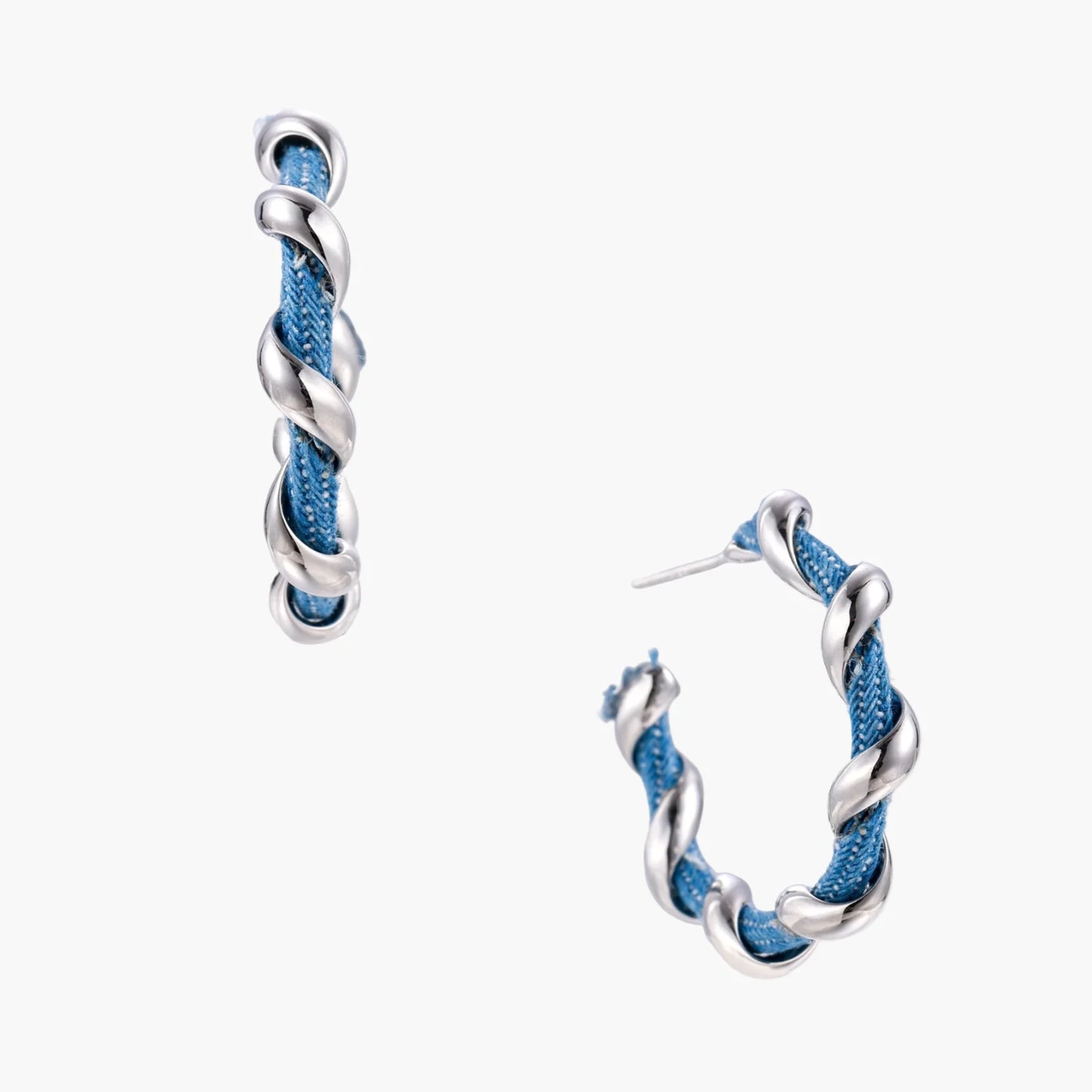 White gold-plated hoops intertwined with blue denim fabric in a twisted rope design on cream background.