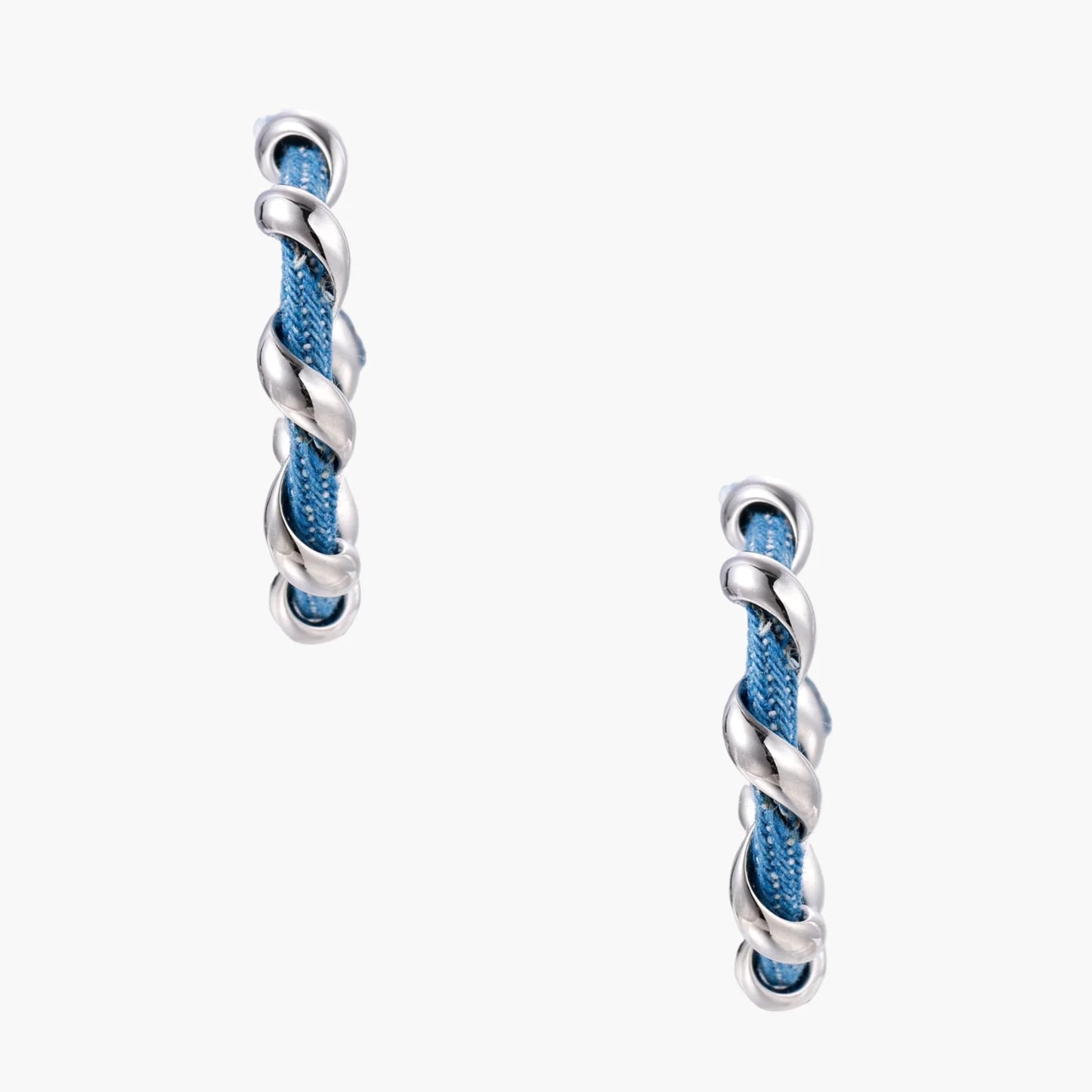 White gold-plated hoops intertwined with blue denim fabric in a twisted rope design on cream background.