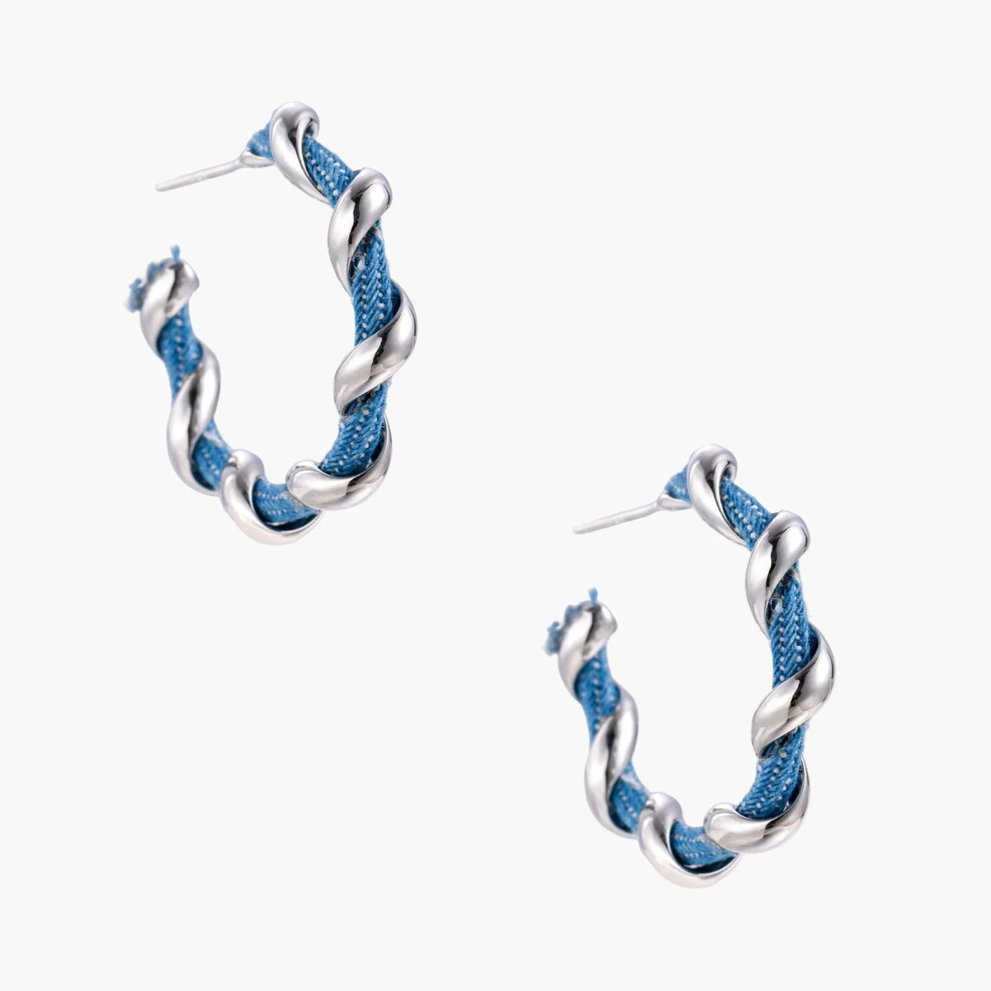 White gold-plated hoops intertwined with blue denim fabric in a twisted rope design on cream background.