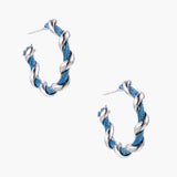 White gold-plated hoops intertwined with blue denim fabric in a twisted rope design on cream background.