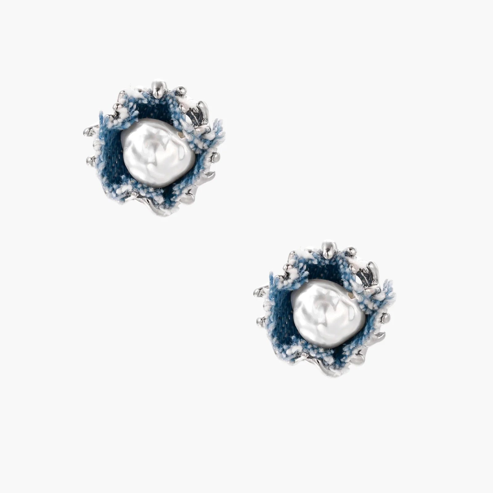 Pair of stud earrings with frayed blue denim petals around white pearl centers and silver prongs on cream background