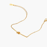 Delicate gold chain bracelet with minimalist bar and centered knot detail on cream background
