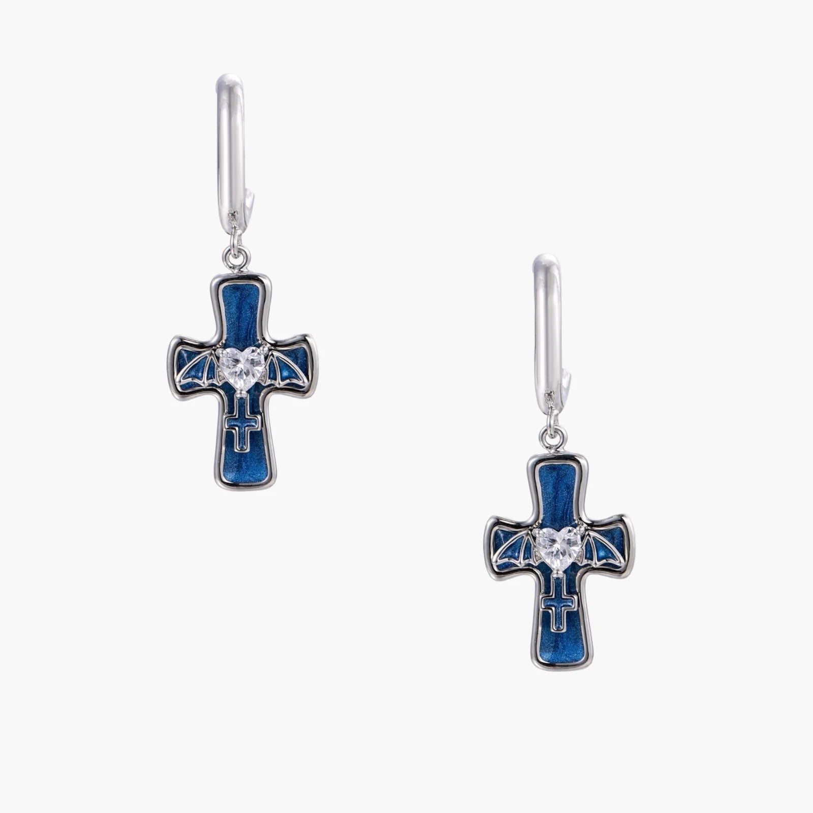 Silver huggie earrings with blue enamel cross charms featuring bat wings and heart-shaped crystal center