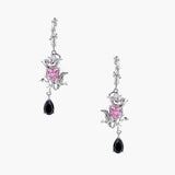 Silver-toned drop earrings with ornate rose design, pink zirconia center, and black teardrop stones on cream background