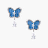 Blue denim butterfly earrings with silver frame and teardrop crystal dangles on cream background