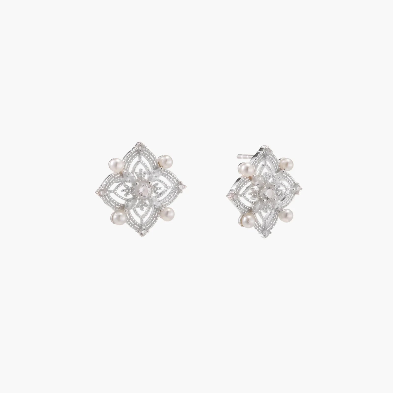 Ornate sterling silver stud earrings with mandala-inspired filigree pattern and four freshwater pearls on beige background
