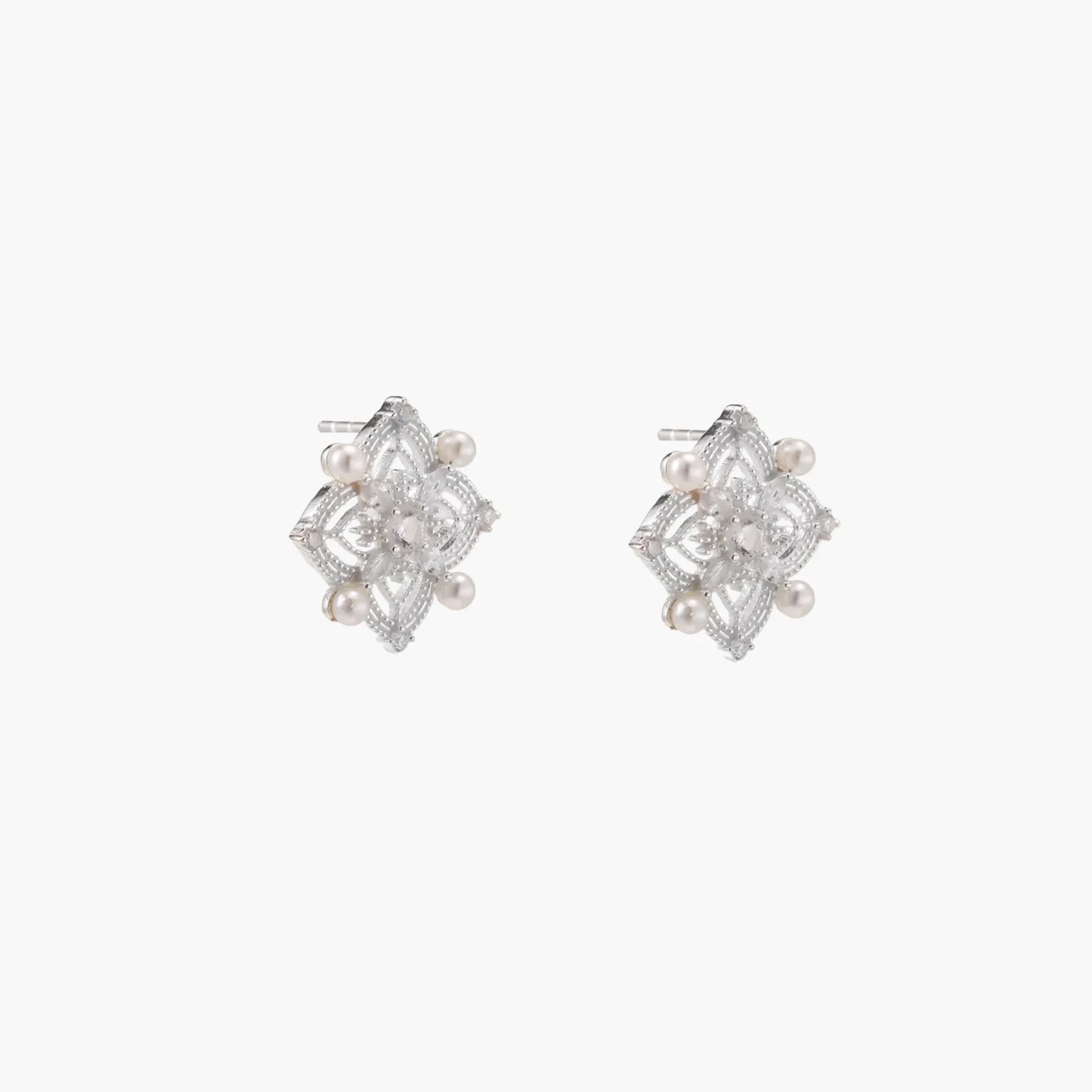 Ornate sterling silver stud earrings with mandala-inspired filigree pattern and four freshwater pearls on beige background