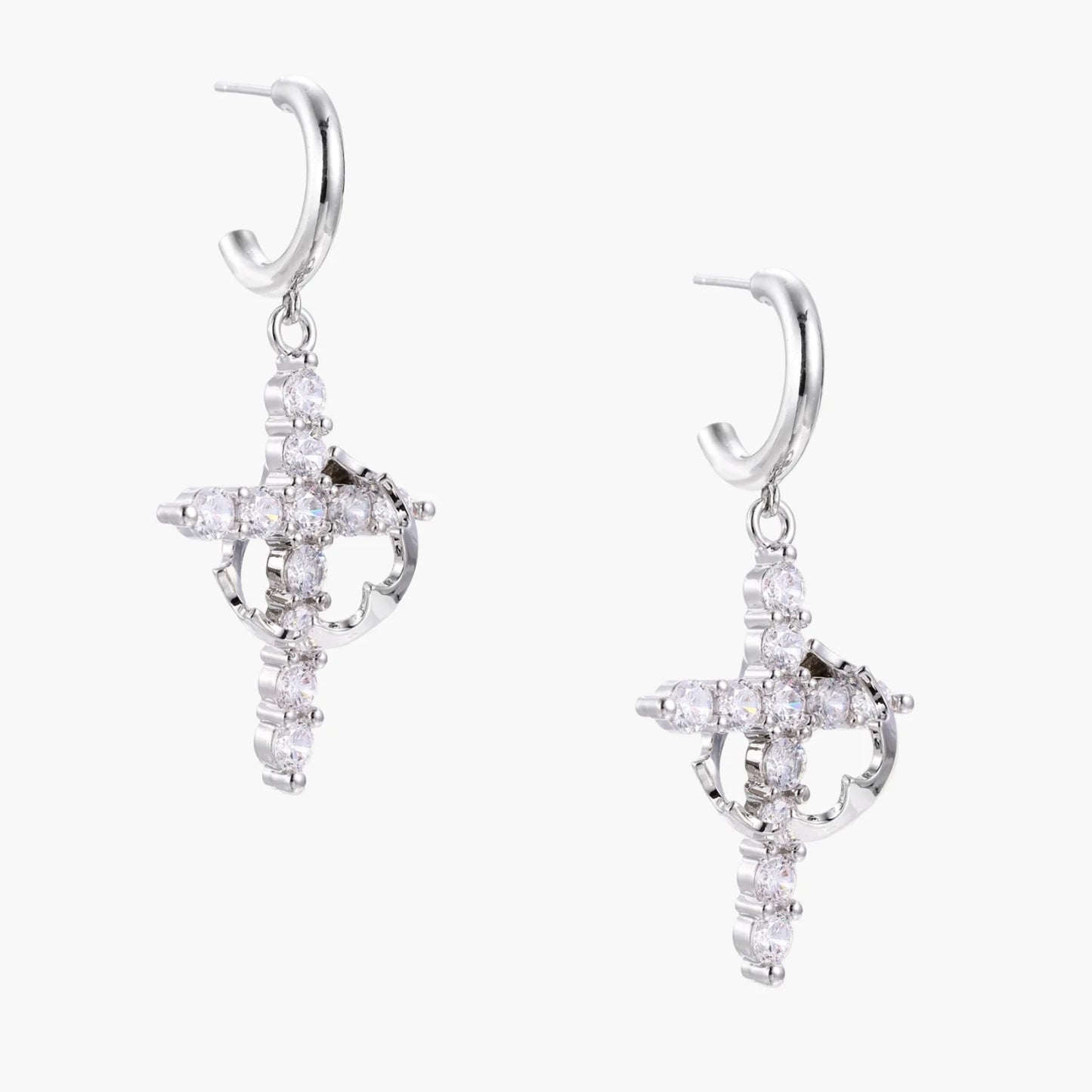 White gold-plated hoop earrings with sparkling zirconia cross charms dangling against cream background