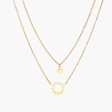 Gold layered necklace set with sunburst and smiley face pendants on delicate chains against white background.