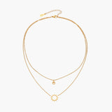 Gold layered necklace set with sunburst and smiley face pendants on delicate chains against white background.