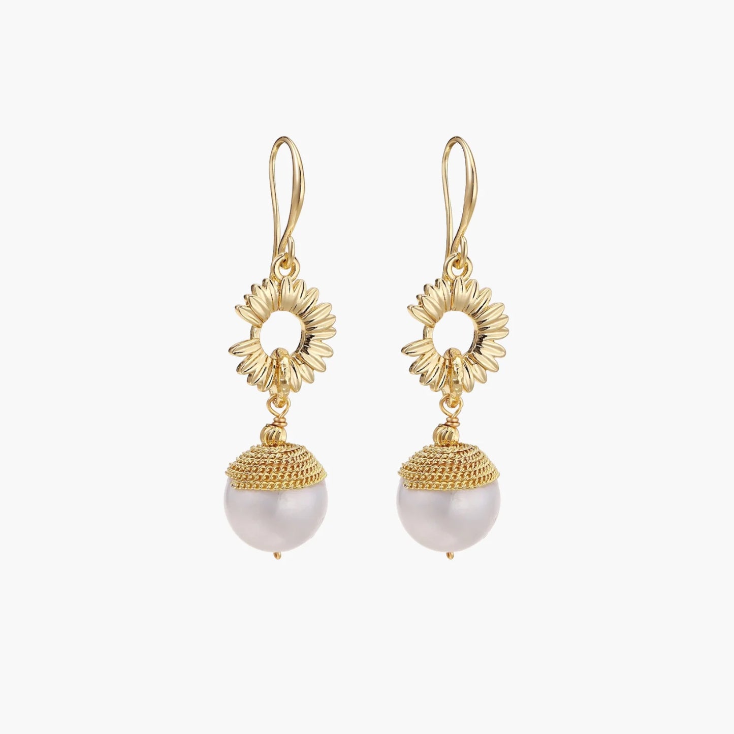 Gold sunburst charm earrings with baroque pearl drops on French hooks against cream background