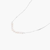 Delicate sterling silver chain necklace with small freshwater pearls arranged in a curved smile arc on cream background.