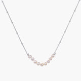 Delicate sterling silver chain necklace with small freshwater pearls arranged in a curved smile arc on cream background.