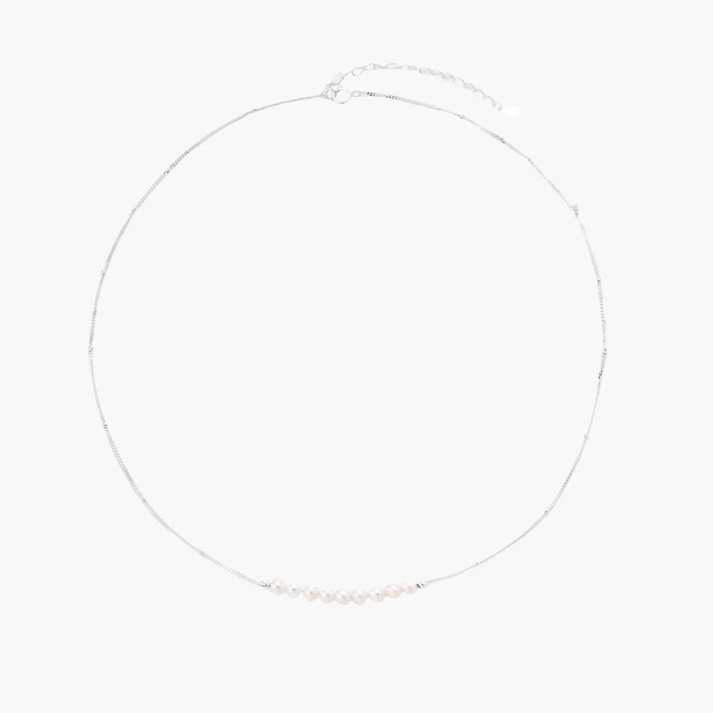 Delicate sterling silver chain necklace with small freshwater pearls arranged in a curved smile arc on cream background.