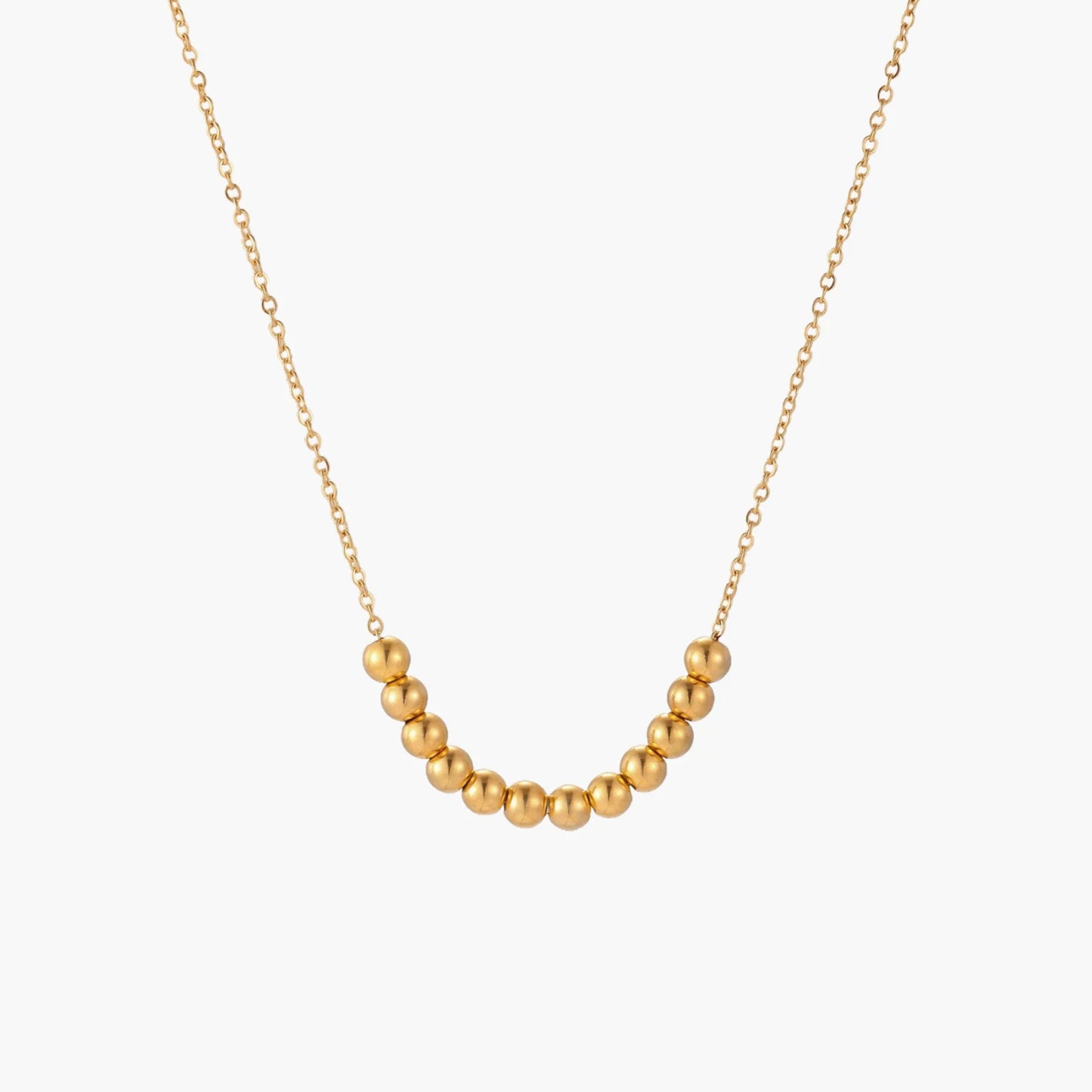 Delicate gold-plated necklace with graduated spherical beads forming gentle smile curve on beige background