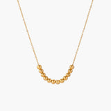 Delicate gold-plated necklace with graduated spherical beads forming gentle smile curve on beige background