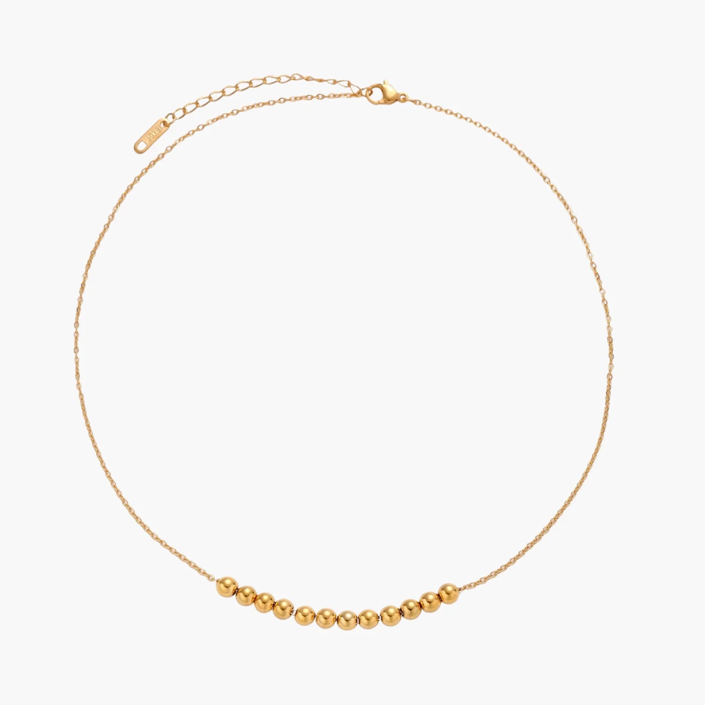 Delicate gold-plated necklace with graduated spherical beads forming gentle smile curve on beige background