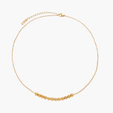Delicate gold-plated necklace with graduated spherical beads forming gentle smile curve on beige background