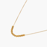 Delicate gold-plated necklace with graduated spherical beads forming gentle smile curve on beige background