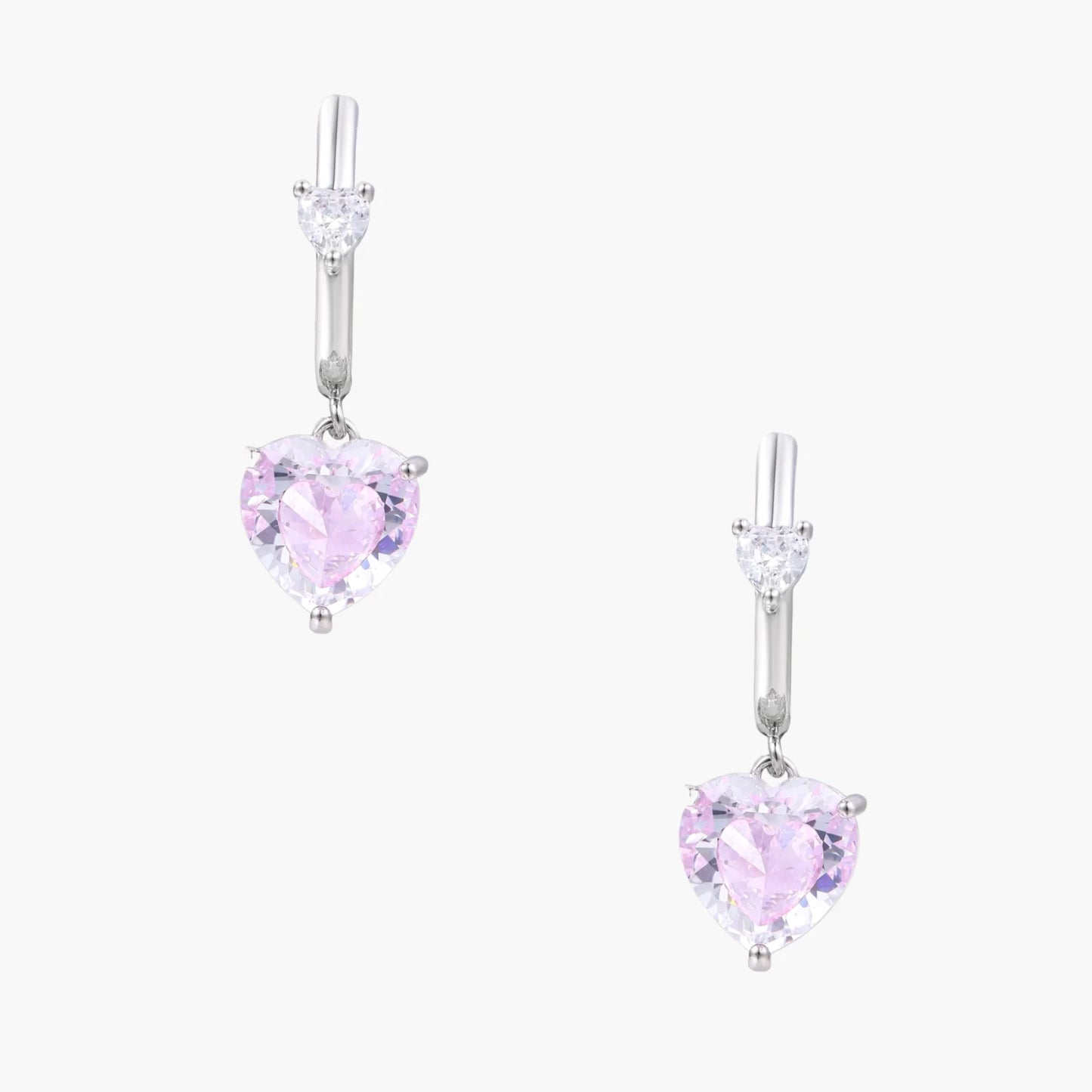 Silver huggie hoops with pink heart-cut zirconia pendants on white background, eco-friendly white gold plated brass