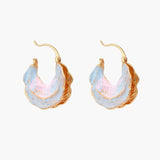 Shell-shaped hoop earrings with iridescent blue-pink enamel and gold trim on cream background