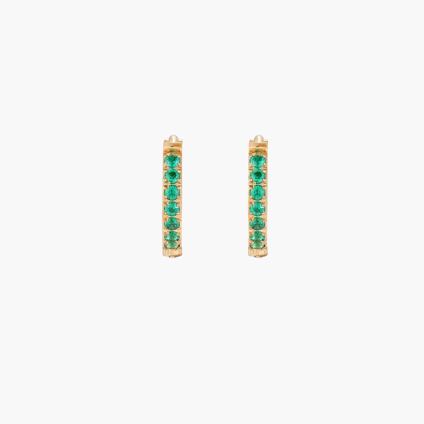 Pair of small gold huggie hoop earrings with bright green cubic zirconia stones on cream background