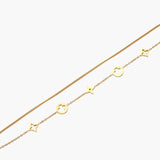 Double-layer gold-plated bracelet with quatrefoil and star charms on cream background, 18K gold finish.