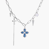 White gold plated chain necklace with blue textured cross pendant, spike charms, and mini cross detail on beige background