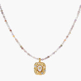 Ornate gold-plated pendant necklace with multicolored gemstone beads in purple, pink and clear tones on white background
