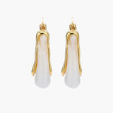 Sculptural gold-plated hoop earrings with flowing curved design and lever-back closure on cream background.