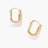 Sculptural gold-plated hoop earrings with flowing curved design and lever-back closure on cream background.