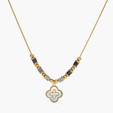 Gold-toned beaded necklace with grey stones and quatrefoil abalone shell pendant on cream background.