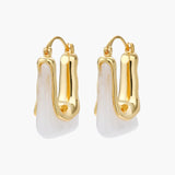 Sculptural gold-plated hoop earrings with flowing curved design and lever-back closure on cream background.